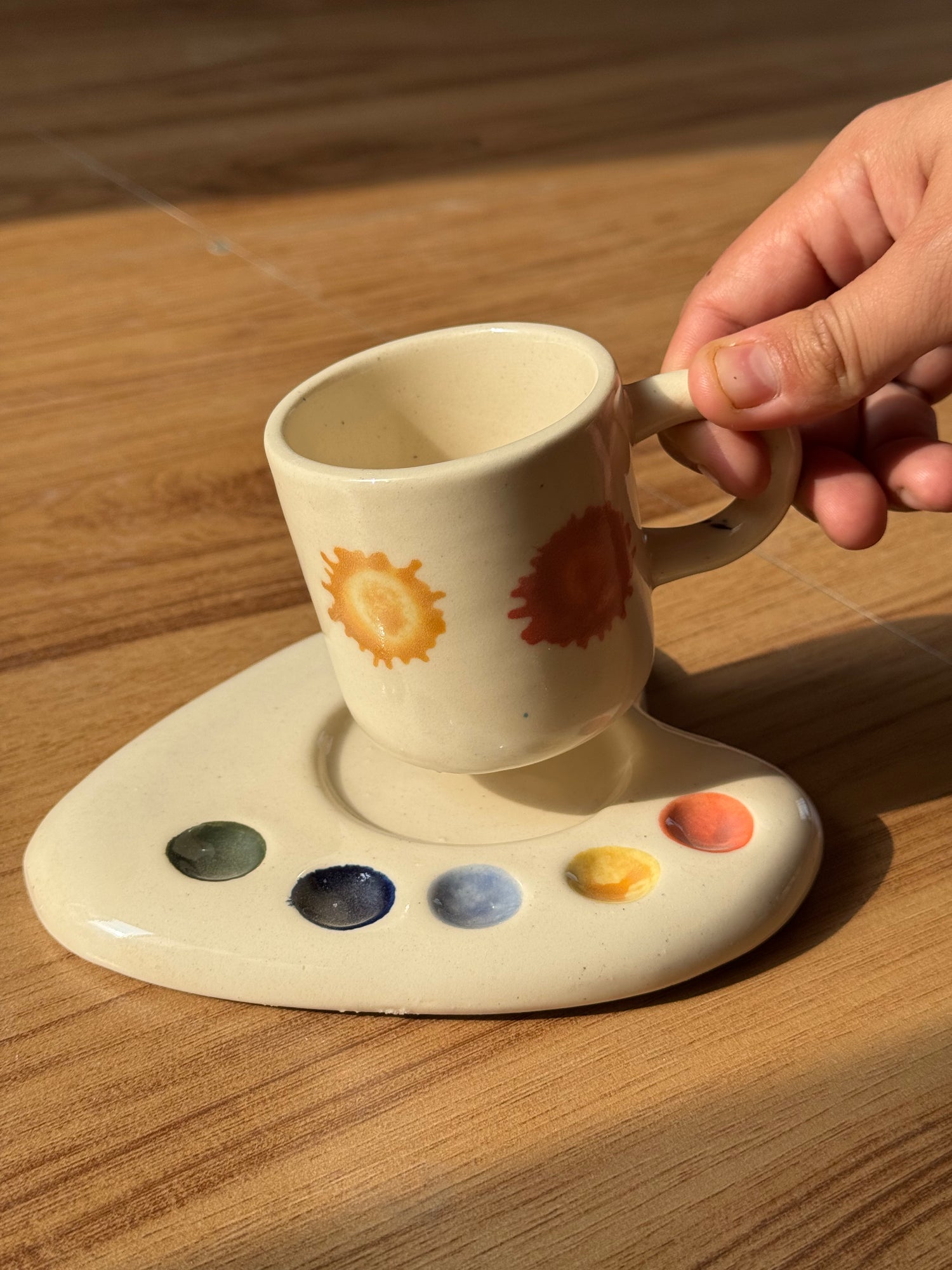 Hand holding the Artist Palette espresso mug above its matching ceramic saucer