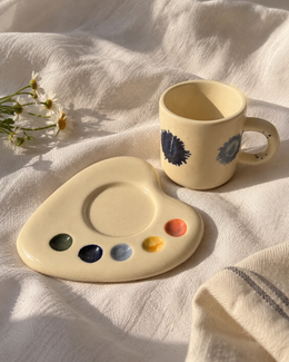 Ceramic espresso mug beside its matching palette-shaped saucer, showing the circular cup recess