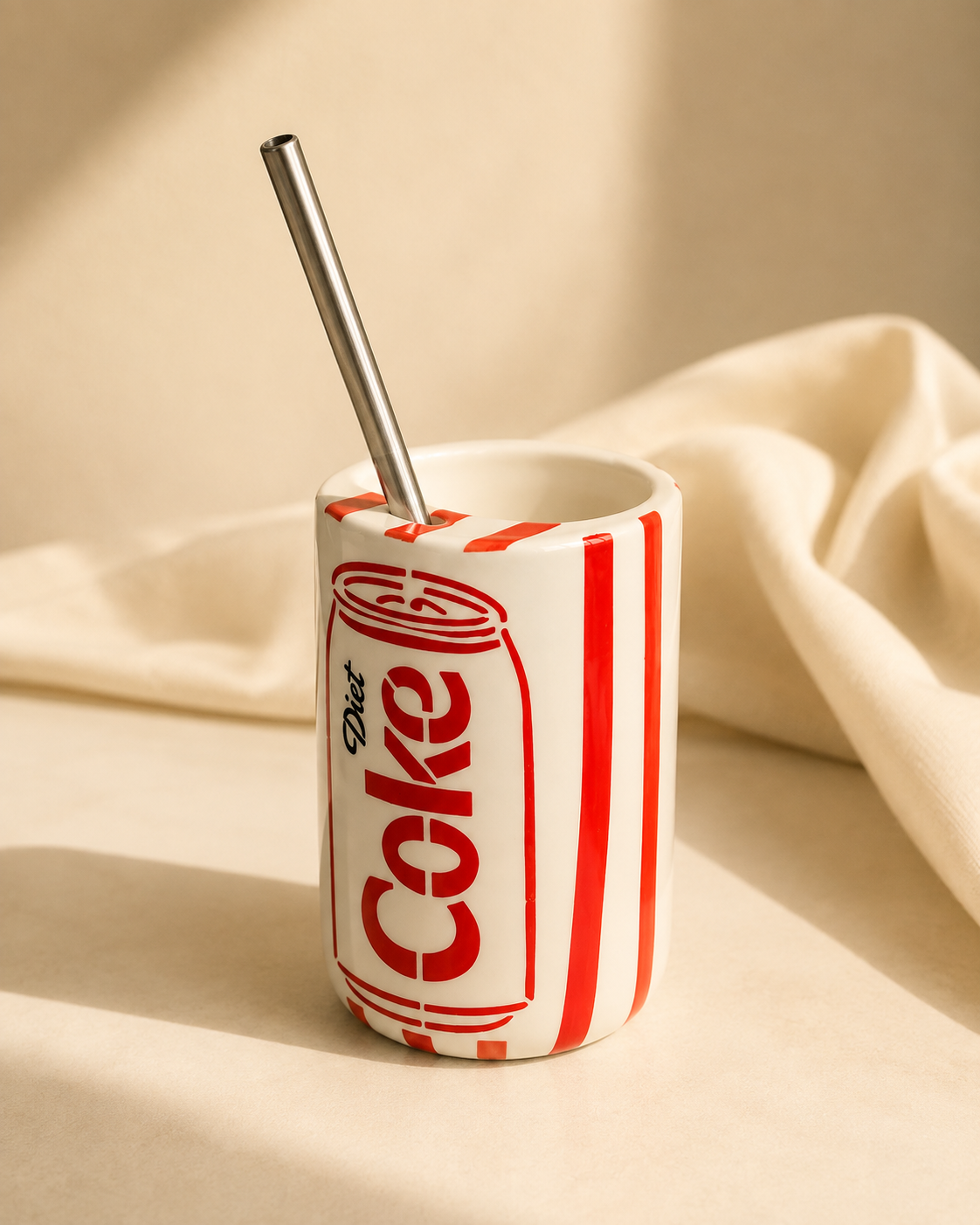 Retro diet cola can-inspired ceramic mug with stainless steel straw on an off-white golden hour background