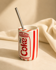 Retro diet cola can-inspired ceramic mug with stainless steel straw on an off-white golden hour background